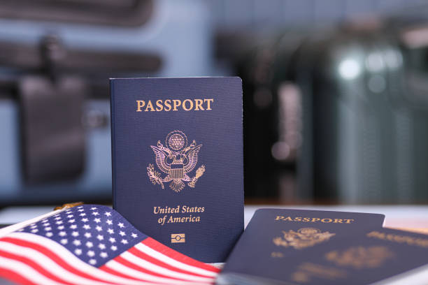 Close-up view of USA passports and American flag with luggage defocused in background. Concepts.\ check passport status