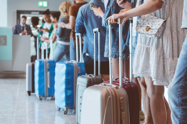 Travelers with luggage using smart phones while waiting in line for boarding at airport. Focus on wheeled luggage.\\ what travelers forget before applying for a passport